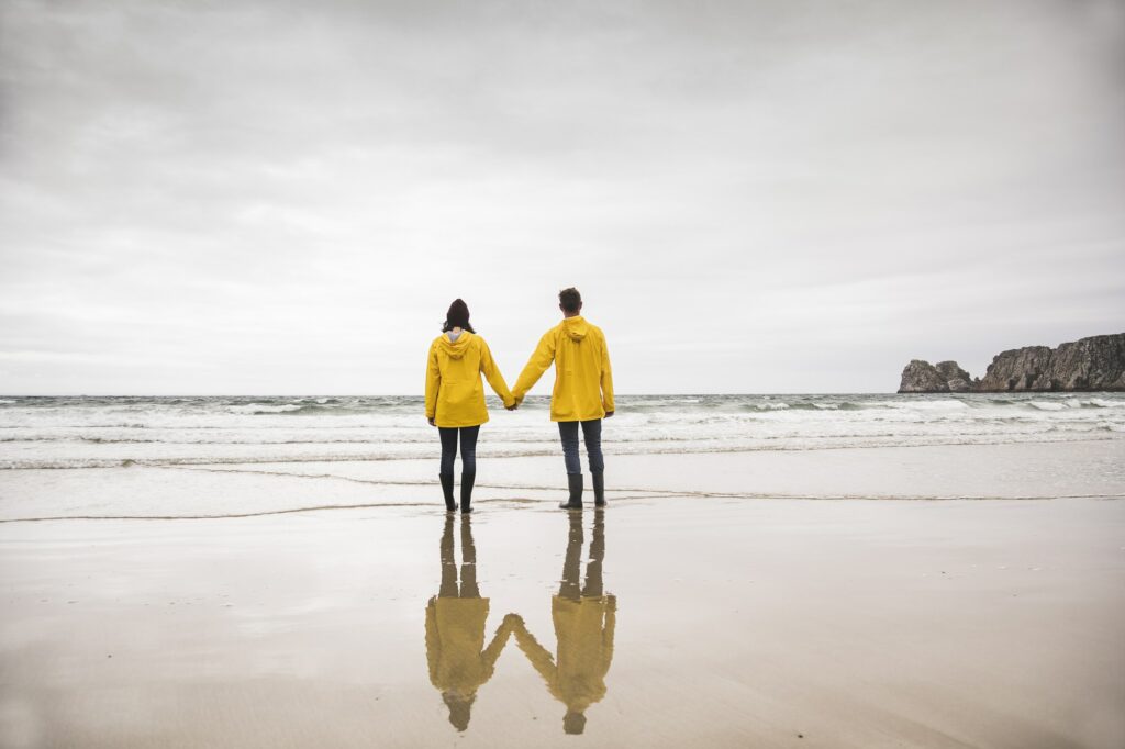 Young woman wearing yellow rain jackets and standing at the beach, Bretagne, France